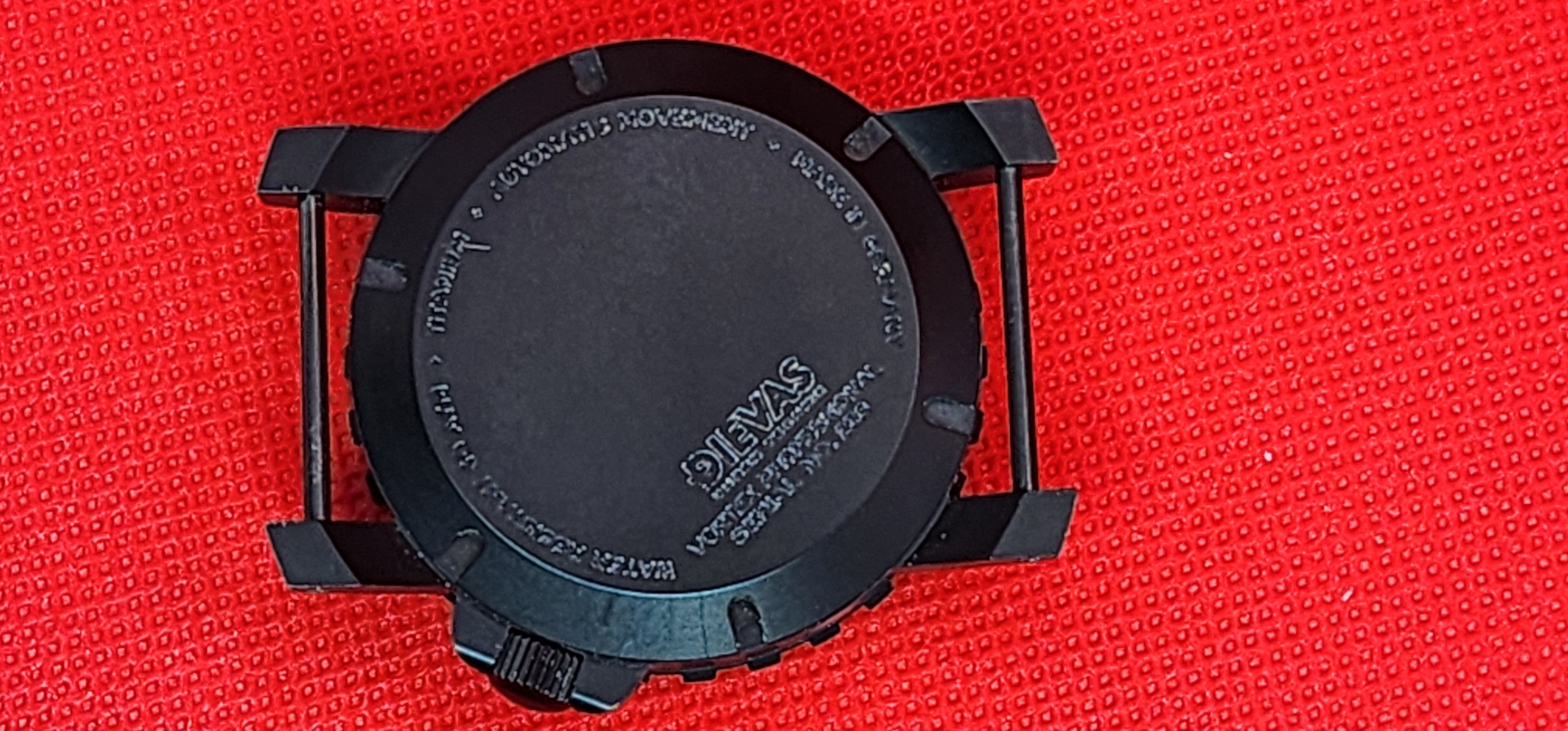 Black round watch case back with a visible 'DIEVAS' logo, photographed on a textured red background.