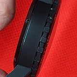 Close-up of a black tactical watch case held between fingers against a bright red textured background.